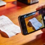 Main tenant prenant en photo un ticket de caisse sur un bureau