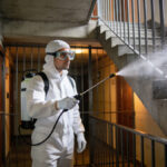 technicien en combinaison blanche pulvérisant insecticide dans cage descalier dimmeuble